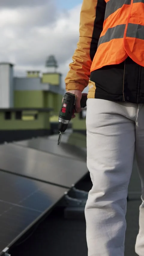 Worker with drill standing on rooftop near solar panels during installation. Stock Footage 321053936