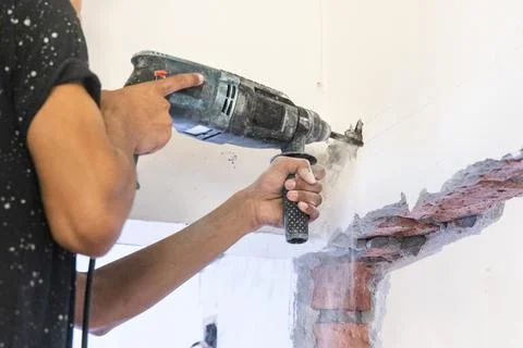 Worker drilling on wall to create cavity for electric power cables in home Foto stock