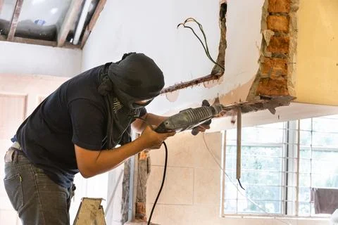 Worker drilling on wall to create cavity for electric power cables in home Stock Photos