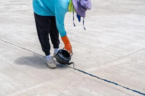 Worker drop asphalt for pot to joint between concrete slab. Stock Photos