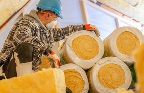 Worker with a dust mask handling attic insulation rolls Photos