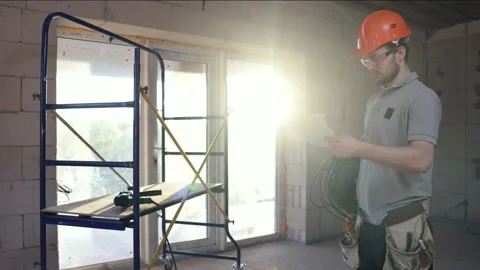 A worker with an electric cable in his hands examines a construction drawing. Stock Footage 158083652