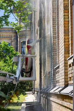 Worker on an elevating platform cleaning the facade of an old brick buildin.. Stock Photos