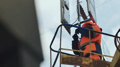A worker in the elevator cradle fixes the LED traffic light. Medium shot. LED Stock Footage 141087324