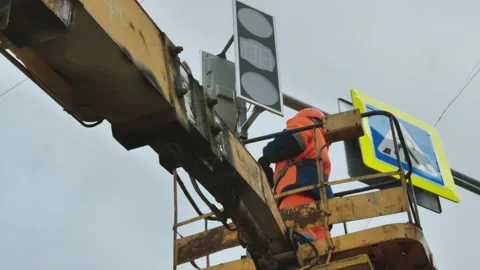 A worker in an elevator cradle repairs an LED traffic light. Road sign. LED Stock-Footage 141078146