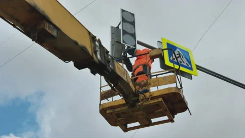 A worker in an elevator cradle repairs an LED traffic light against a background Stock Footage 141132224