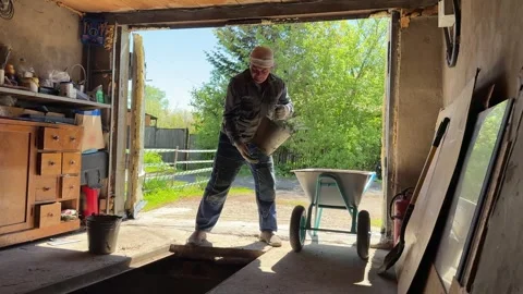 Worker emptying bucket of dirt into wheelbarrow during garage inspection pit 库存影片 337989653