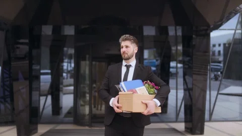 Worker experiences layoffs while carrying personal items outside office building Stock Footage 307038664