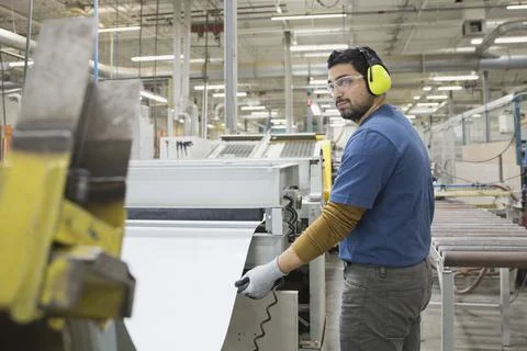 Worker extracting steel sheet from machine in factory Stock Photos
