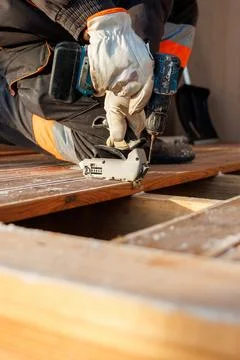 Worker fastens grooved deck board with drill on frosted timber joists Stock Photos