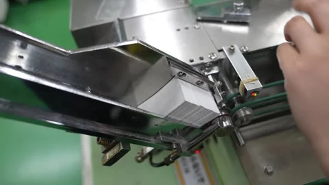Worker feeding white paint tubes into a labelling machine on a green production 動画素材 347124237