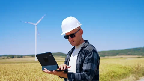 Worker in field using tablet near wind turbine on sunny day. A worker stands in Video stock 342737233