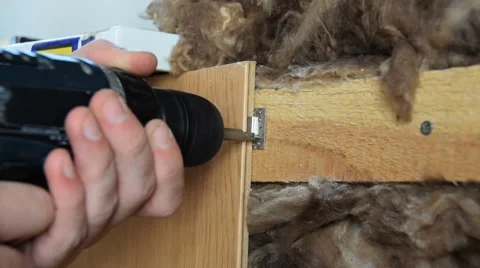 Worker fixes board to wall using electric screwdriver. Mineral wool under board. Stock Footage 64734515