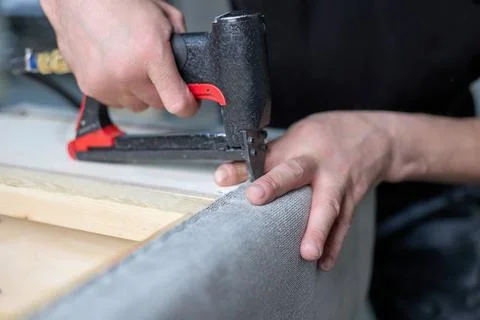 Worker fixes the fabric with a pneumatic stapler in the factory shop. Stock Photos