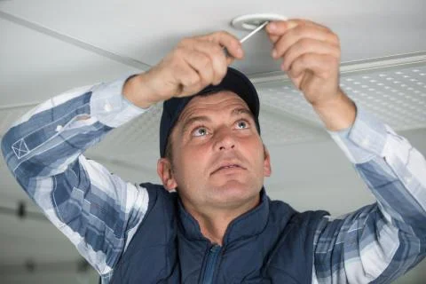 Worker fixes the lamp to the ceiling with a screwdriver Stock Photos