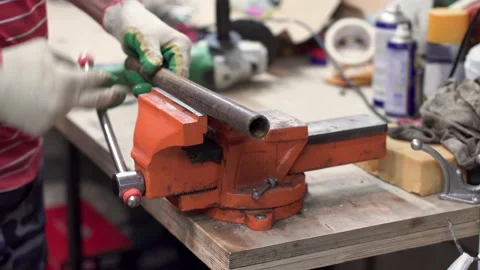 A worker fixes a metal pipe in red locksmith vice and takes a grinder. workshop Stock Footage 147617196
