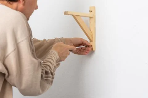 A worker fixes screws on a shelf corner with a screwdriver Foto stock