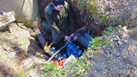 Worker fixes water pump in underground location during sunny day Stock Footage 337425796