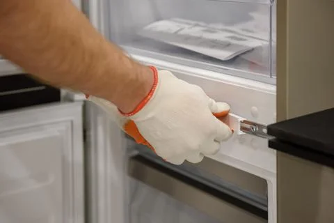A worker is fixing the built-in refrigerator in the kitchen furniture. Stock Photos