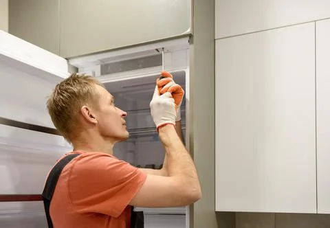 The worker is fixing the built-in refrigerator in the kitchen furniture. Stock Photos