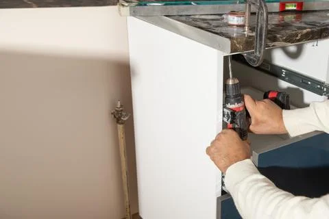 Worker fixing kitchen cabinet using cordless screwdriver. Stock Photos