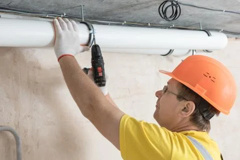 The worker is fixing ventilation pipes. Stock Photos