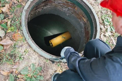 A worker with a flashlight inspects an open sewer manhole. Septic tank main.. Stockfoto's