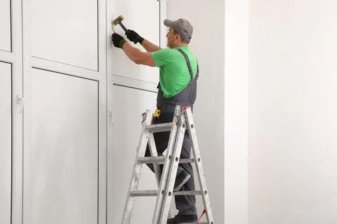 Worker on folding ladder installing window indoors Stock Photos