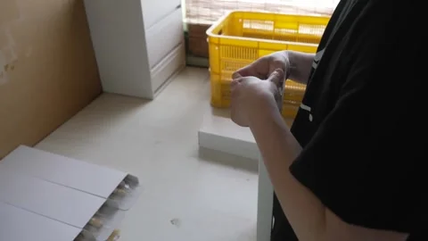 Worker folding white cardboard packaging boxes beside a yellow plastic crate in Stock Footage 341593913