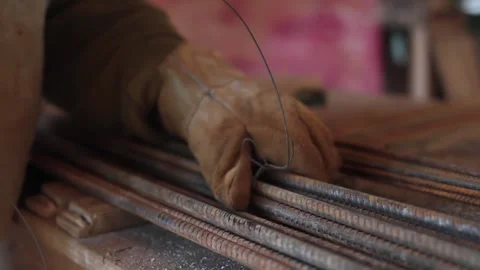 Worker gathering rebars with a wire, and using gloves at construction site Stock Footage 255684461