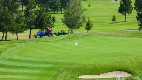 A worker gets into a lawn mower and cuts the grass on a golf course. Stock Footage 262237518