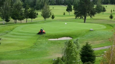 A worker gets into a lawn mower and cuts the grass on a golf course. Stock Footage 263921501