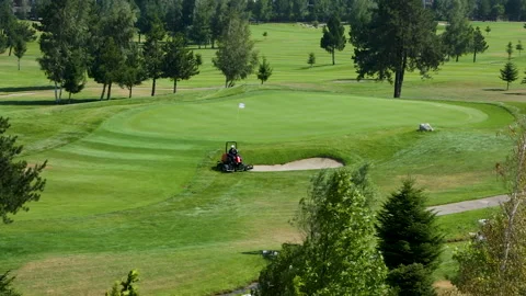 A worker gets into a lawn mower and cuts the grass on a golf course. Stock Footage 264786044