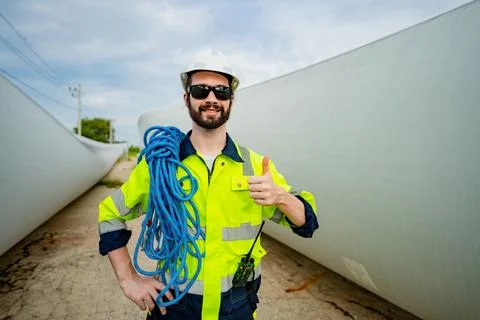 Worker giving thumbs up while standing near large wind turbine blades at a .. Stock Photos