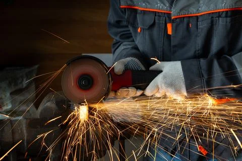 A worker in gloves cutting metal with an angle grinder tool in a workshop 스톡 사진