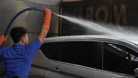 Worker with gloves using hose to wash a vehicle in professional car wash station 스톡 동영상 199649256