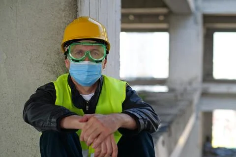 Worker in goggles and protective mask sits at construction site, looks at cam Foto stock