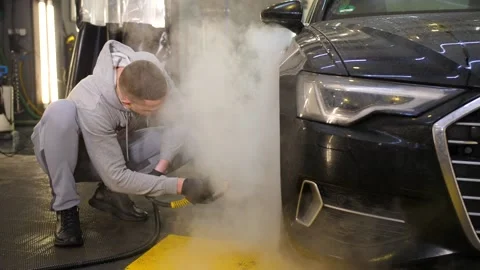 A worker in gray clothes cleans the front wheel of a black car with a hot steam Video stock 169540070