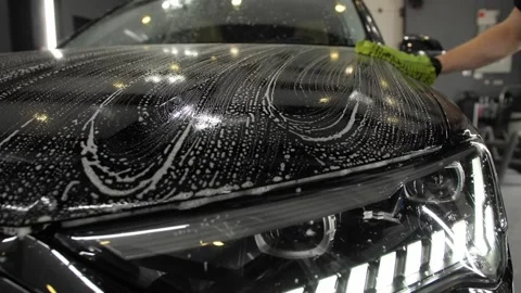 A worker with a green sponge cleaning foam hood and car headlight. Stock Footage 247239000