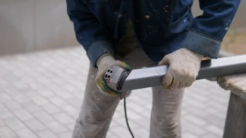 Worker grinding rectangular metal tube outdoors with handheld tool, bright Stock-Footage 344873639
