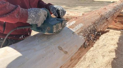 Worker grinds a log with an electric tool. Preparation for building a house. Stock Photos
