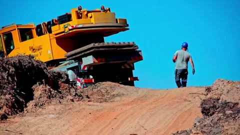 Worker guiding crane truck while reversing on dirt road at construction site Stock Footage 334337850
