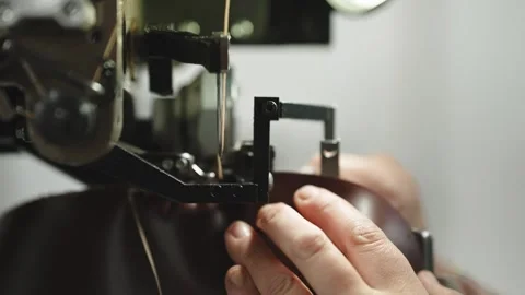 Worker guiding dark leather shoe sole under stitching machine needle Stock Footage 333015994