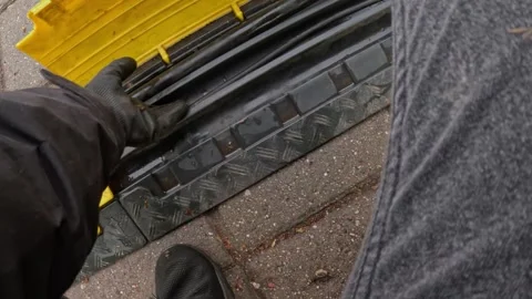 Worker guiding power cable into protective ramp on pavement during setup Stock Footage 312658327