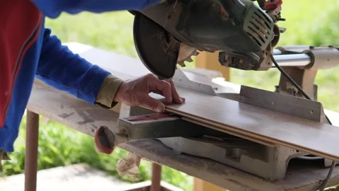 Worker guiding powered miter saw through wooden boards on rustic outdoor Stock Footage 344872706