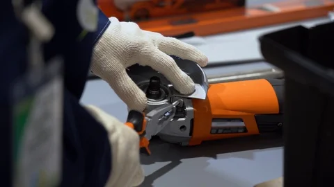 Worker guy uses plier tool, repairs an orange electric grinder on a metal table Stock Footage 126356060