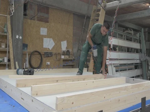 Worker hammering nails in beams by using pneumatic gun at worktable. Stock Footage 79950364