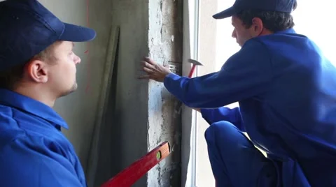 Worker hammers dowel fixing bracket on jamb. Another one stands near Stock Footage 50282465