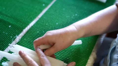Worker hand gathering a cluster of thin white taper candles from a green mesh Stock Footage 343370644