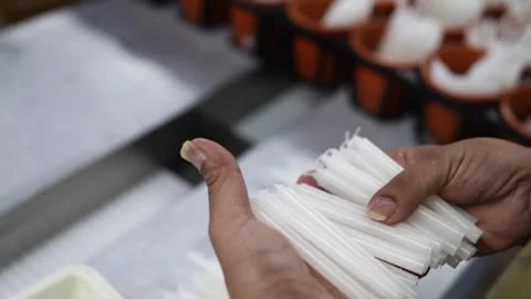 Worker hand holding a bundle of thin white wax rods beside orange candle molds Stock Footage 343875721